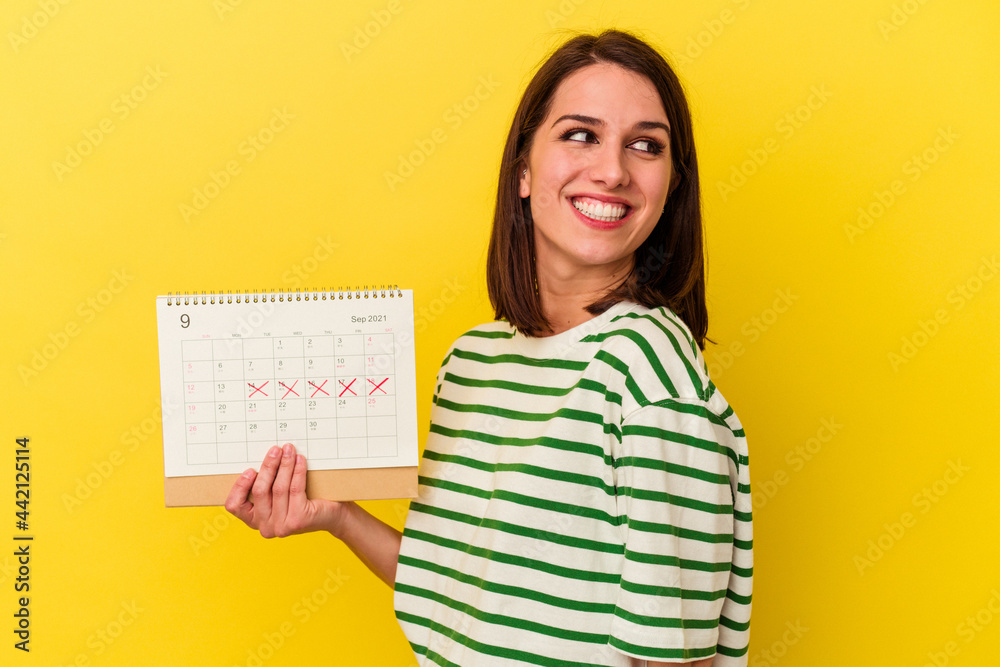 Young australian woman holding a calendar isolated on yellow background looks aside smiling, cheerful and pleasant. Young australian woman holding a calendar isolated on yellow background looks aside smiling, cheerful and pleasant.