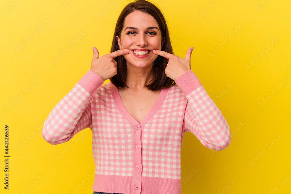 Young caucasian woman isolated on yellow background smiles, pointing fingers at mouth. Young caucasian woman isolated on yellow background smiles, pointing fingers at mouth.