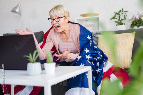 Old American lady watching games, cheering with an American flag suppotting her team. photo