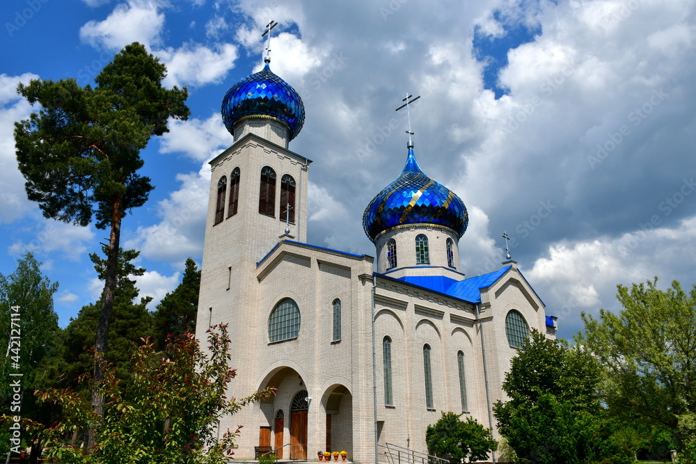 Close up on old Orthodox church standing in the middle of a dense forest or moor with its towers and dome covered with a blue reflective metal shining in the sun seen on a cloudy summer day in Poland