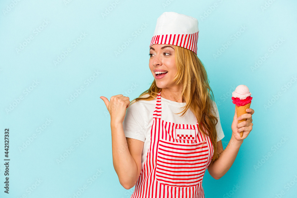 Caucasian ice cream maker woman holding an ice cream isolated on blue background points with thumb finger away, laughing and carefree. Caucasian ice cream maker woman holding an ice cream isolated on blue background points with thumb finger away, laughing and carefree.