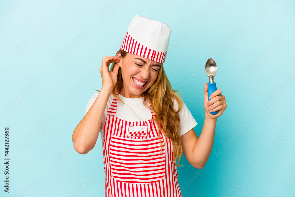 Caucasian ice cream maker woman holding an ice cream scoop isolated on blue background covering ears with hands. Caucasian ice cream maker woman holding an ice cream scoop isolated on blue background covering ears with hands.
