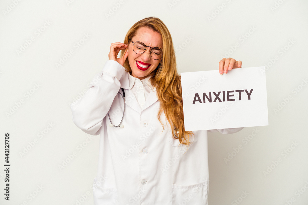 Caucasian doctor woman holding a anxiety placard isolated on white background covering ears with hands. Caucasian doctor woman holding a anxiety placard isolated on white background covering ears with hands.