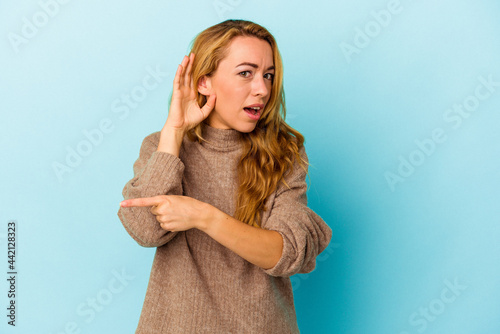 Caucasian woman isolated on blue background trying to listening a gossip.