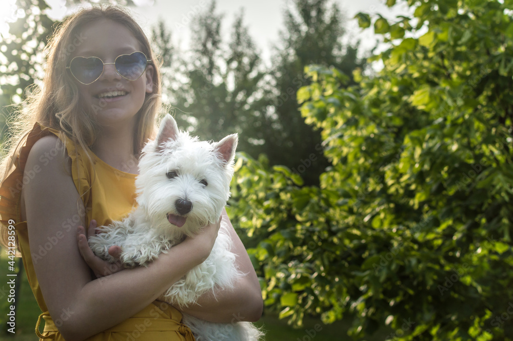 Portrait of a happy teenage girl in sunglasses with her white terrier dog in the summer in the park Portrait of a happy teenage girl in sunglasses with her white terrier dog in the summer in the park