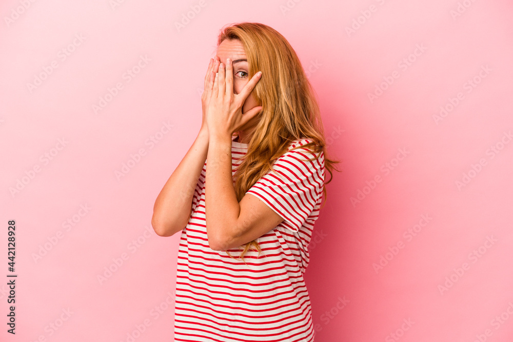 Caucasian blonde woman isolated on pink background blink through fingers frightened and nervous.