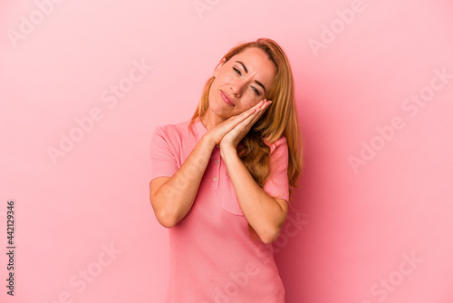 Caucasian blonde woman isolated on pink background yawning showing a tired gesture covering mouth with hand.