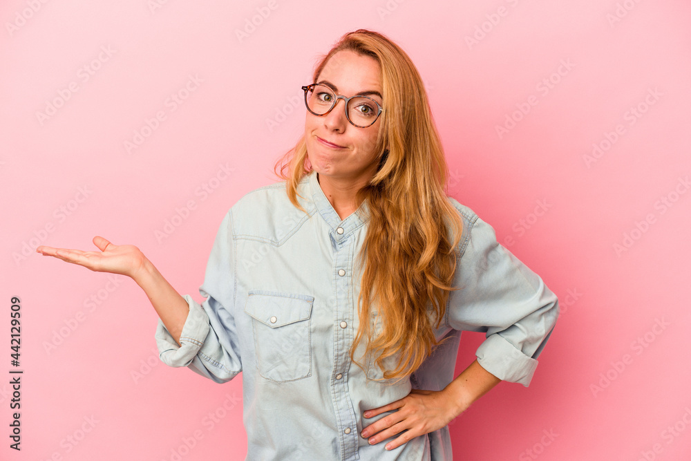 Caucasian blonde woman isolated on pink background showing a copy space on a palm and holding another hand on waist. Caucasian blonde woman isolated on pink background showing a copy space on a palm and holding another hand on waist.