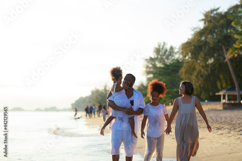 Happy African american family holding hands and walking together on the beach during holiday.