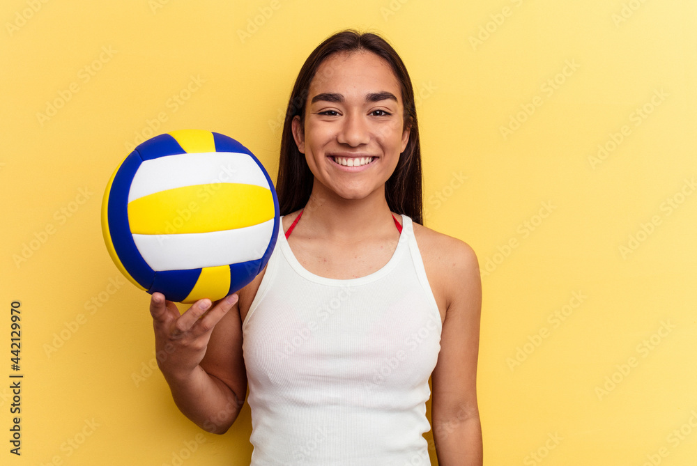 Young mixed race woman playing volleyball on the beach isolated on yellow background happy, smiling and cheerful.