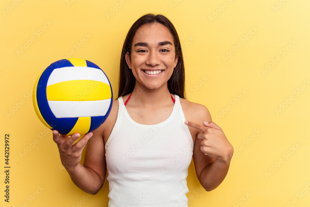 Young mixed race woman playing volleyball on the beach isolated on yellow background person pointing by hand to a shirt copy space, proud and confident