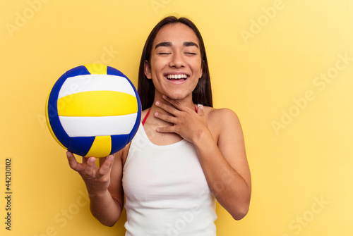 Young mixed race woman playing volleyball on the beach isolated on yellow background laughs out loudly keeping hand on chest.