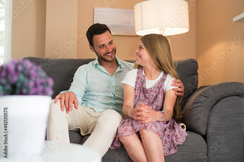 A shot of a father and daughter sitting on a sofa and smiling.