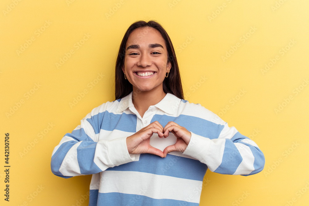 Young mixed race woman isolated on yellow background smiling and showing a heart shape with hands. Young mixed race woman isolated on yellow background smiling and showing a heart shape with hands.