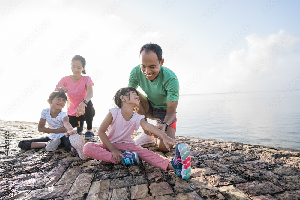 father and mother help their daughter to stretch the leg during exercising outdoor