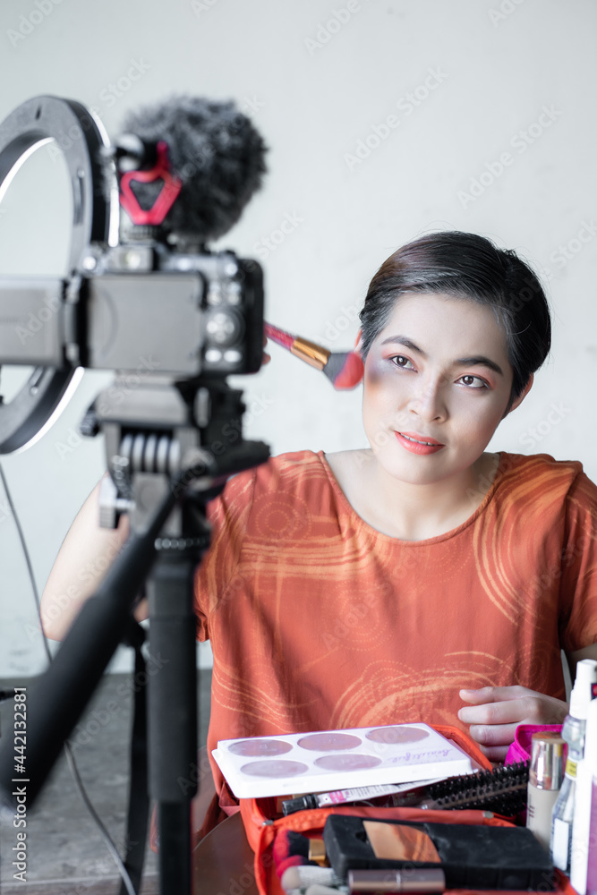 Asian beautiful fashion beauty blogger looks into a digital camera. reviews beauty product for video blog,  talking on cosmetics holding a makeup palette while recording her video.