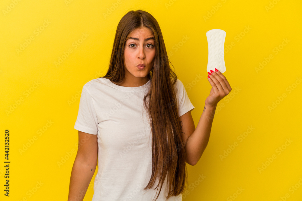 Young caucasian woman holding a compress isolated on yellow background shrugs shoulders and open eyes confused. Young caucasian woman holding a compress isolated on yellow background shrugs shoulders and open eyes confused.