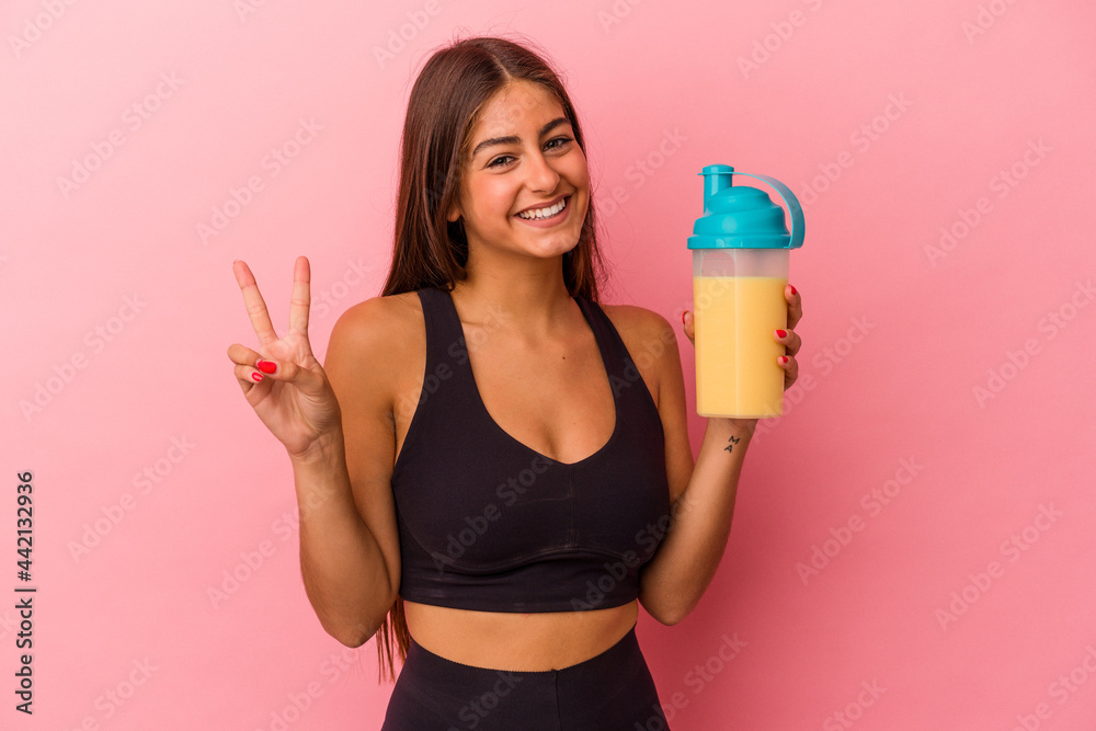 Young caucasian woman holding a protein shake isolated on yellow background joyful and carefree showing a peace symbol with fingers. Young caucasian woman holding a protein shake isolated on yellow background joyful and carefree showing a peace symbol with fingers.