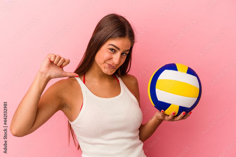 Young caucasian woman holding a volleyball ball isolated on pink background feels proud and self confident, example to follow.