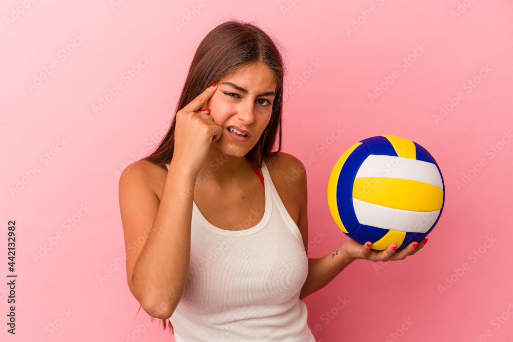 Young caucasian woman holding a volleyball ball isolated on pink background showing a disappointment gesture with forefinger.
