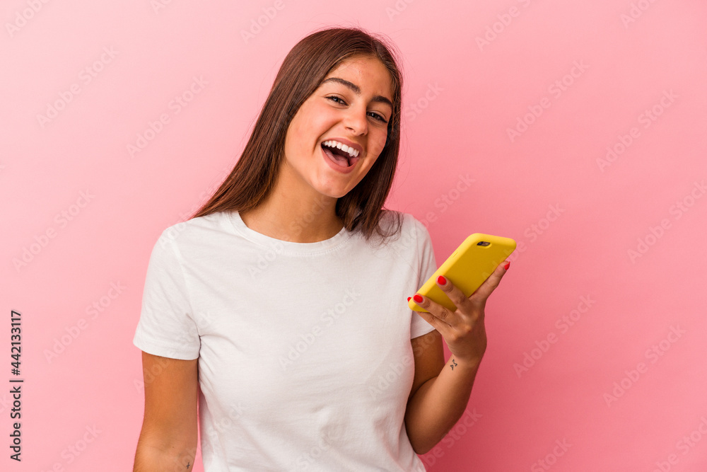 Young caucasian woman holding a mobile phone isolated on pink background laughing and having fun. Young caucasian woman holding a mobile phone isolated on pink background laughing and having fun.