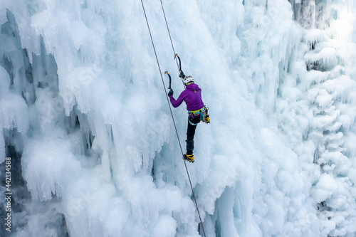 Female ice climber climbing up the side of an icy slope with bumps, ridges, and icicles