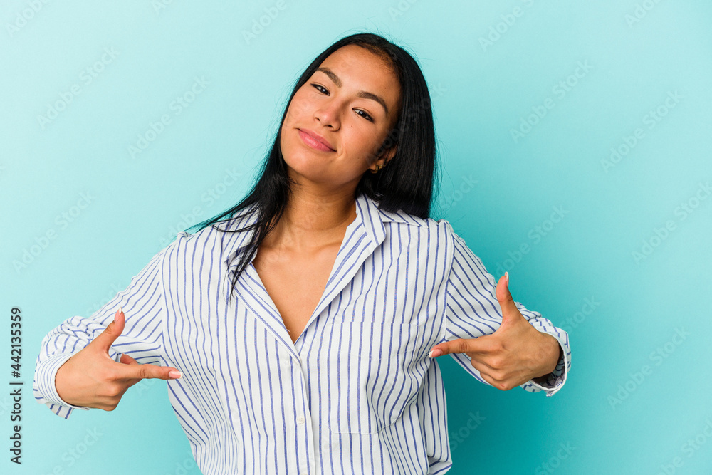 Young Venezuelan woman isolated on blue background person pointing by hand to a shirt copy space, proud and confident Young Venezuelan woman isolated on blue background person pointing by hand to a shirt copy space, proud and confident