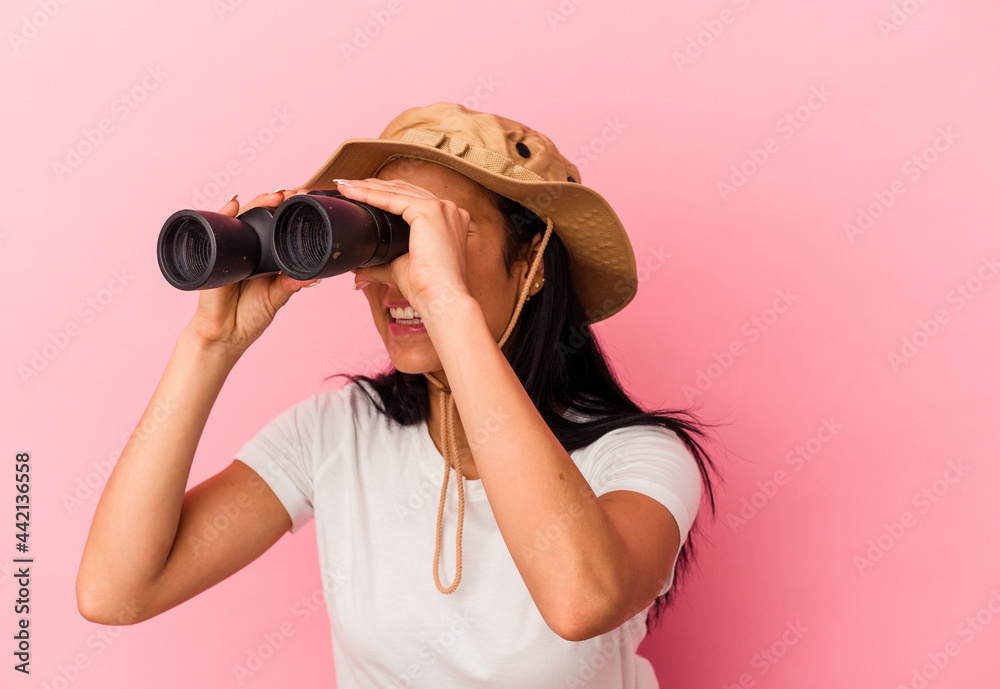 Young mixed race explorer woman holding binoculars isolated on pink background Young mixed race explorer woman holding binoculars isolated on pink background