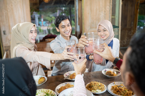 group of young asian people celebrating and raising glasses of fruit ice for toast while breaking fast together in the dining room