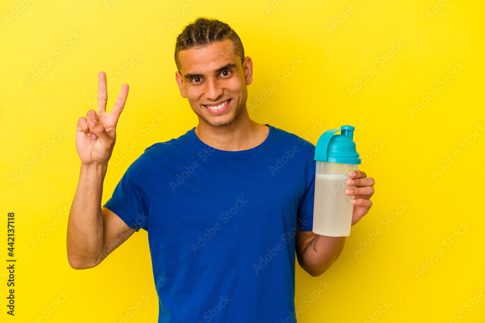 Young venezuelan man drinking a protein shake isolated on yellow background showing number two with fingers.