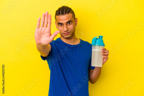Young venezuelan man drinking a protein shake isolated on yellow background standing with outstretched hand showing stop sign, preventing you.