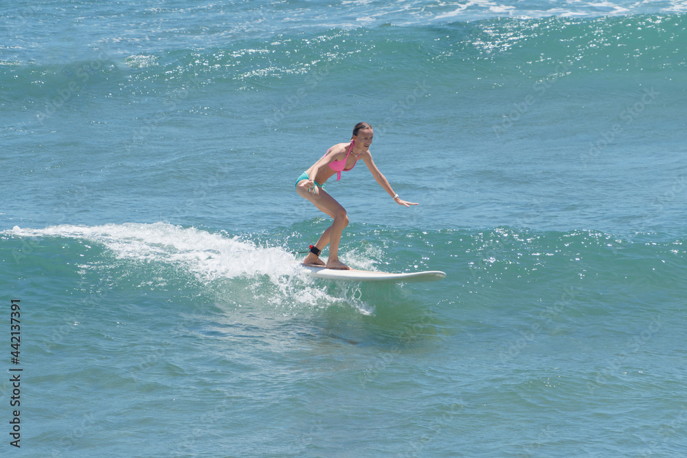 Female surfer wearing pink bikini riding on wave at sunny day in tropical water. Active lifestyle.