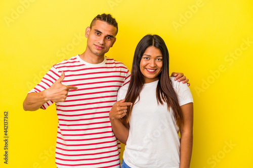 Young latin couple isolated on yellow background person pointing by hand to a shirt copy space, proud and confident
