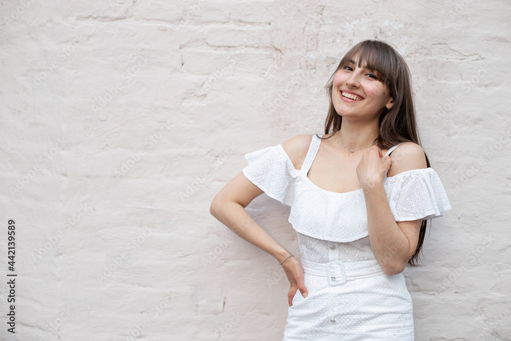 smiling brunette girl with long hair in a white dress on solid brick background. place for your design smiling brunette girl with long hair in a white dress on solid brick background. place for your design