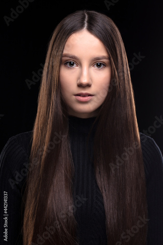 Beautiful brunette girl with long hair on a black background. Seventeen-year-old woman. Classic portrait of a young girl.