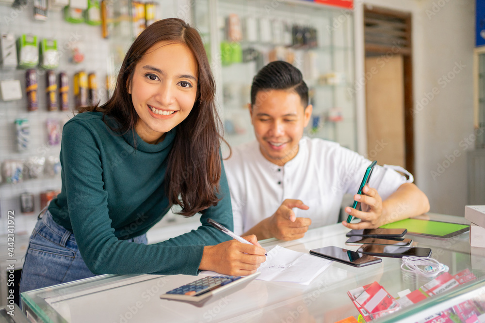beautiful woman shop assistant smiling while working with a man checking goods note paper with notes on mobile against glass display case background in smartphone shop beautiful woman shop assistant smiling while working with a man checking goods note paper with notes on mobile against glass display case background in smartphone shop