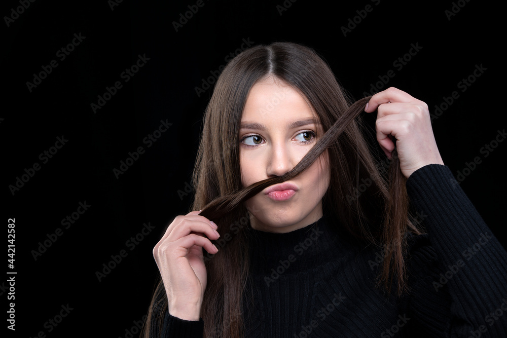 Obraz premium A beautiful girl with long hair fooling around in front of the camera. Makes a mustache out of hair.