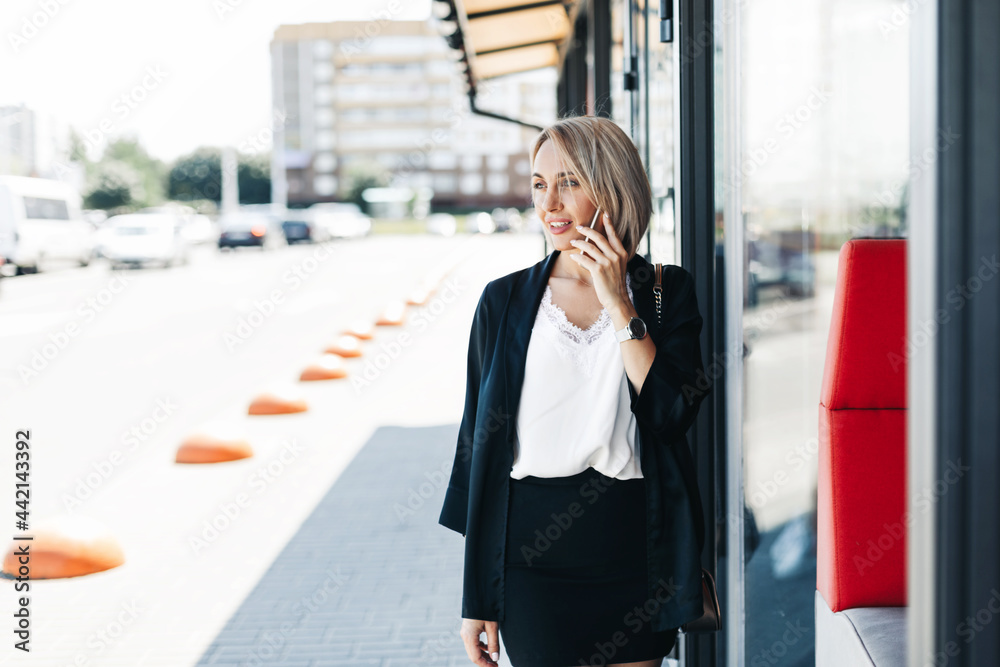 Fototapeta premium A beautiful businesswoman, talking on the phone in the city, holding a folder with documents