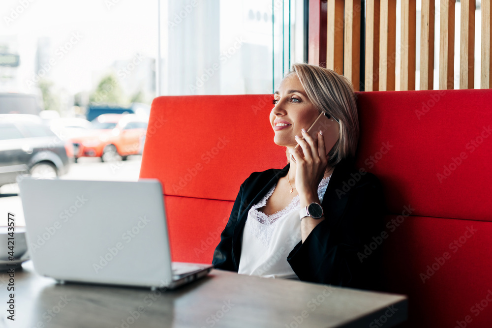 Obraz premium An attractive girl is talking on a mobile phone and smiling, sitting alone in a cafe