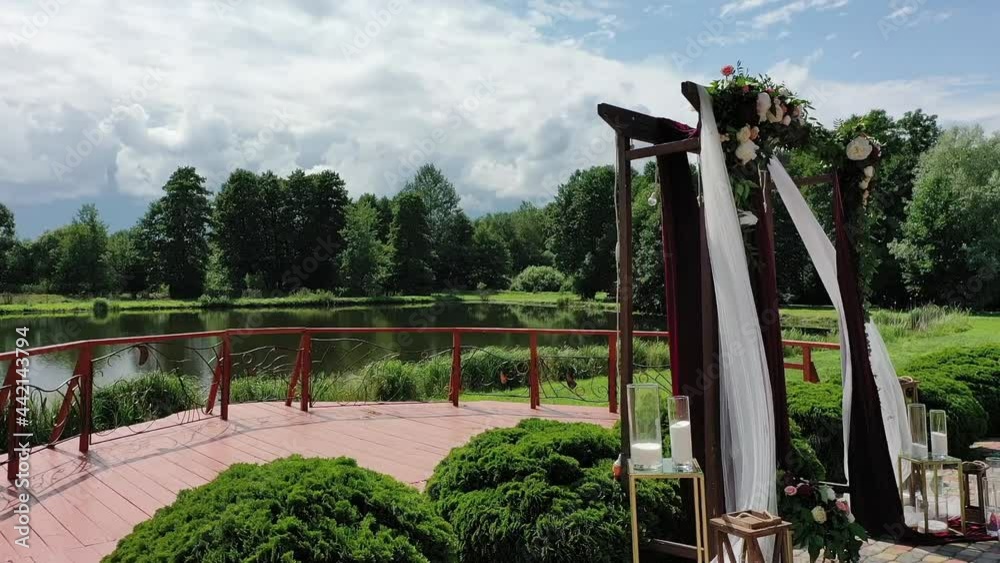 Beautiful Ceremonial Wedding Altar on the pond bank. Romantic place among beautiful nature. Decoration and wedding organizations service. Drone view, pan Beautiful Ceremonial Wedding Altar on the pond bank. Romantic place among beautiful nature. Decoration and wedding organizations service. Drone view, pan