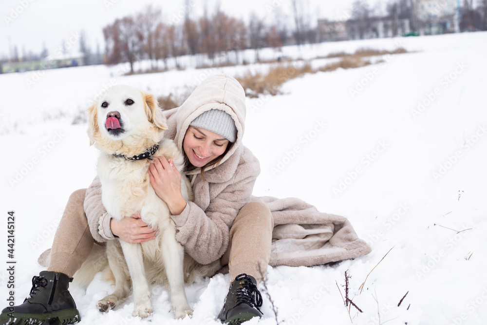 Young beautiful woman and her golden retriever dog having fun in winter.
