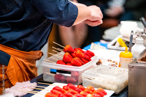 Kyoto, Japan fruit food vendor preparing strawberry skewers on sale display in Nishiki market street