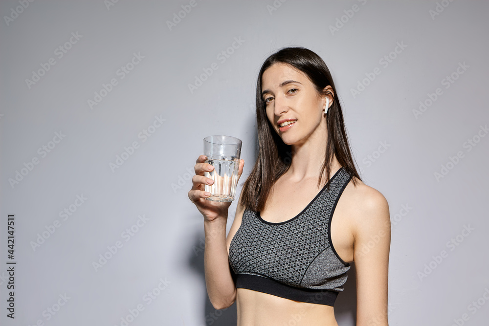 A woman in sports clothes and with wireless headphones drinks water. the concept of a healthy lifestyle and sports activities A woman in sports clothes and with wireless headphones drinks water. the concept of a healthy lifestyle and sports activities