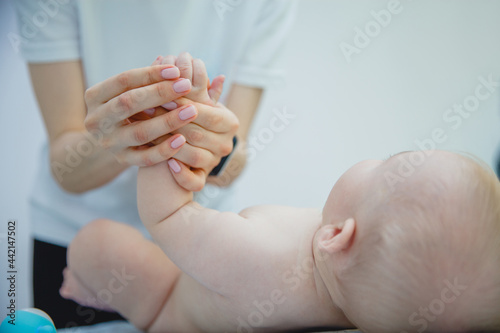 a female masseur in a white T-shirt gives a massage of the handles to a baby in a massage room