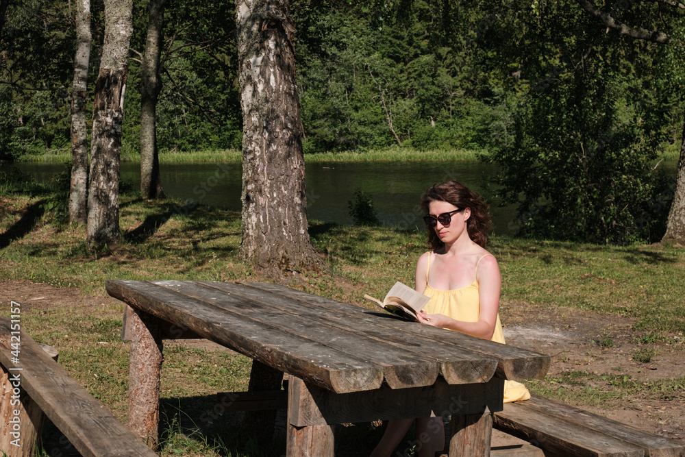 Fototapeta premium The girl sits at the table and reads a book. Education outside the city