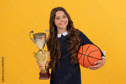 happy teen girl hold basketball ball and champion cup on yellow background, champion photo