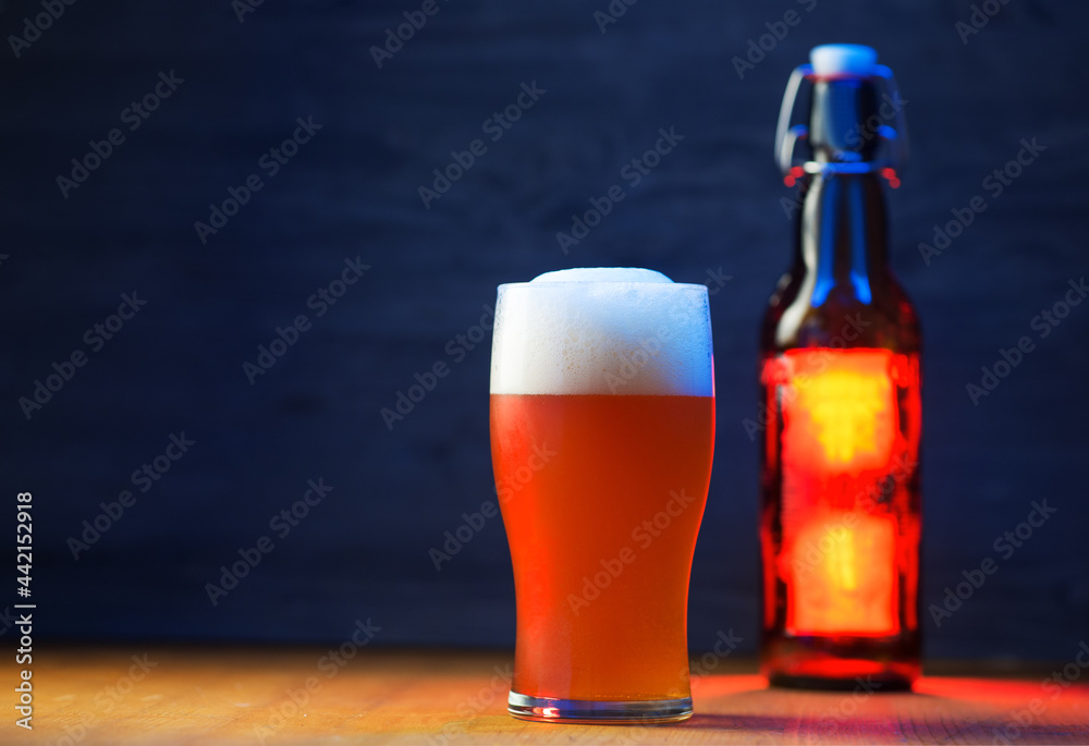 A tall glass of a pint of beer on a wooden table, a beer bottle with a bugle stopper. Unfiltered traditional wheat beer, copy space, blue backlight - obrazy, fototapety, plakaty 