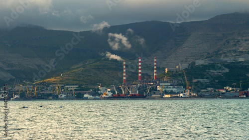 Industrial enterprise. Sea port. Port cranes. Sea shore. Smoke from chimneys. Rocky mountains in the background. It's a nasty day. Panorama. Ecology. Pollution.