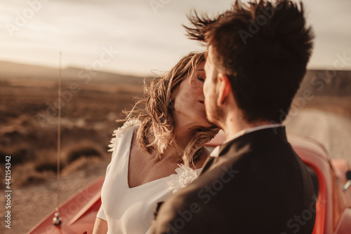 Newlyweds kissing near sports car in desert photo