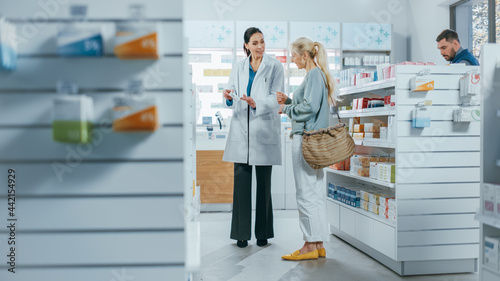Pharmacy  Professional Pharmacist Helping Beautiful Senior Female Customer with Medicine Recommendation  Advice  Talking. Drugstore with Full of Drugs Packages  Pills Bottles  Health Care Products